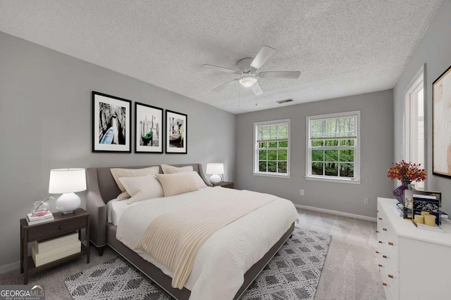 bedroom with visible vents, baseboards, a textured ceiling, light colored carpet, and ceiling fan