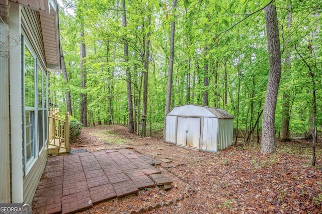 view of yard featuring an outdoor structure, a storage unit, a view of trees, and a patio