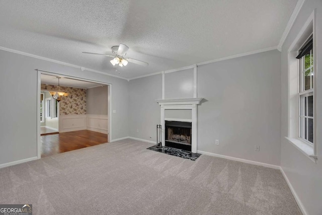 unfurnished living room with a fireplace with flush hearth, carpet flooring, wainscoting, ceiling fan with notable chandelier, and ornamental molding