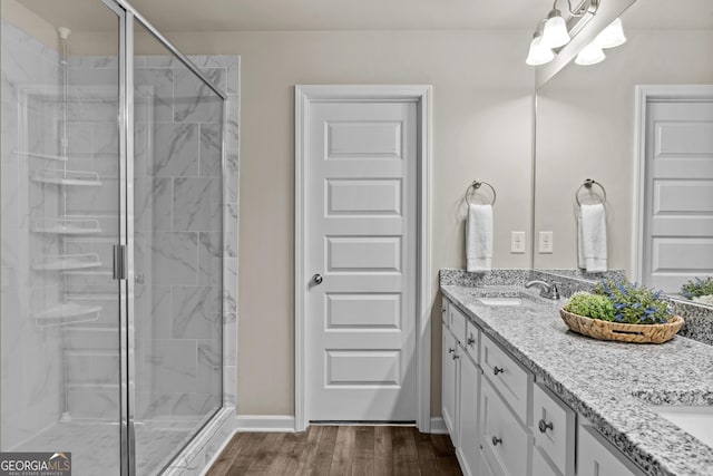 bathroom with a shower stall, double vanity, wood finished floors, a sink, and a chandelier