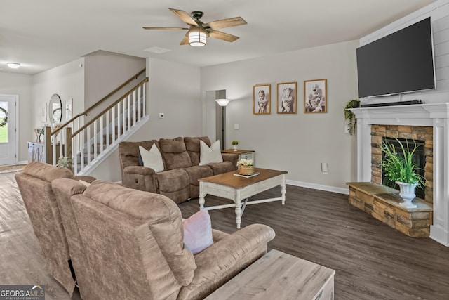 living room featuring wood finished floors, a stone fireplace, a ceiling fan, baseboards, and stairs