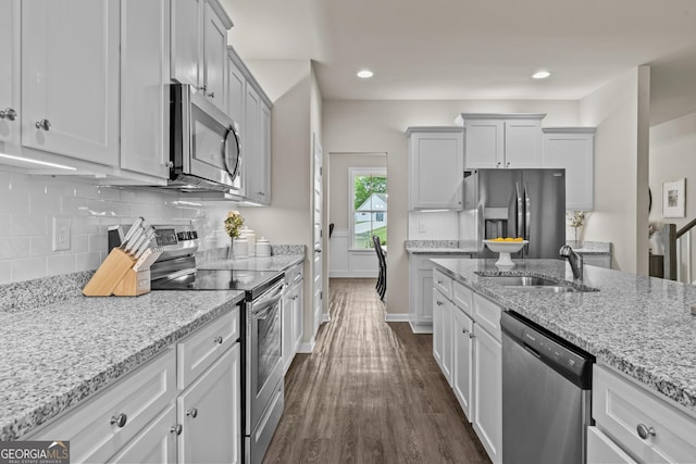kitchen with stainless steel appliances, a sink, dark wood-type flooring, light stone countertops, and tasteful backsplash