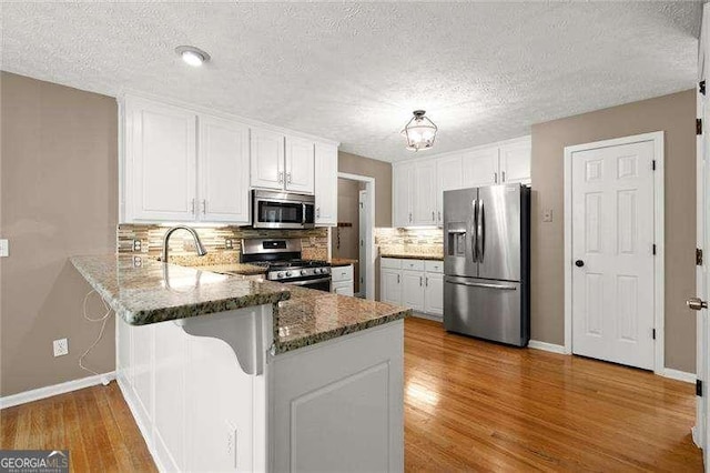 kitchen featuring stone countertops, decorative backsplash, a peninsula, appliances with stainless steel finishes, and white cabinetry