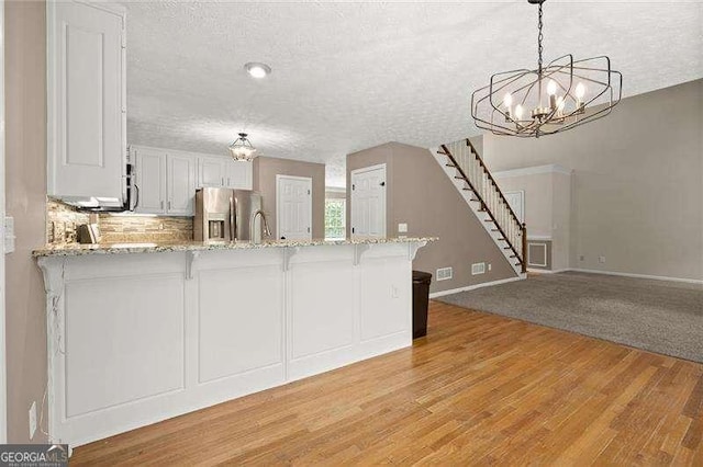 kitchen featuring stainless steel refrigerator with ice dispenser, a peninsula, a notable chandelier, and a kitchen breakfast bar