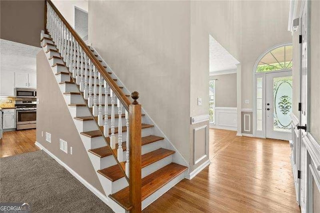 entrance foyer with stairway, a decorative wall, light wood-type flooring, a wainscoted wall, and a towering ceiling
