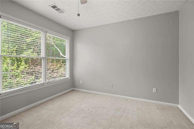 unfurnished room featuring a textured ceiling, ceiling fan, light carpet, baseboards, and visible vents