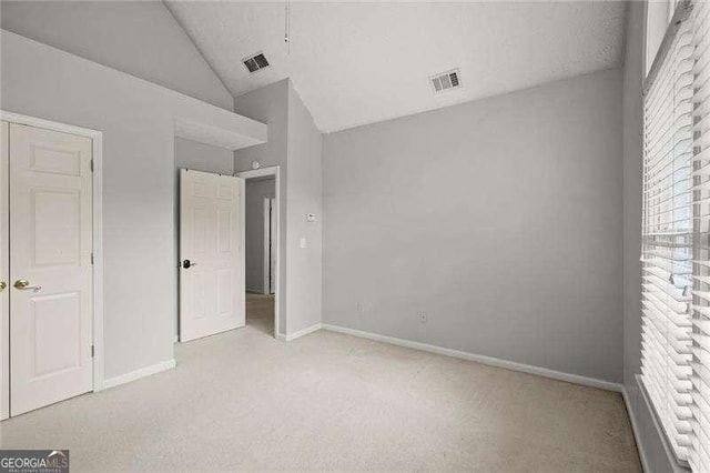 unfurnished bedroom with lofted ceiling, baseboards, visible vents, and light colored carpet