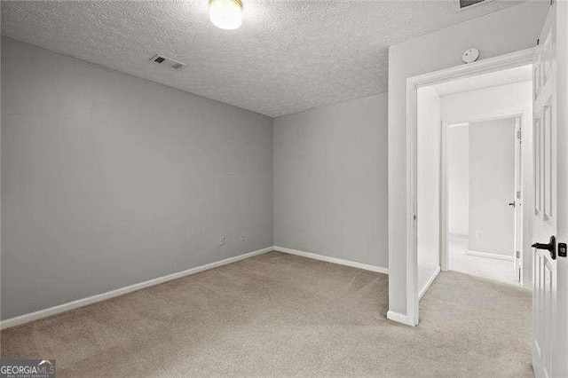 empty room featuring a textured ceiling, baseboards, visible vents, and light colored carpet