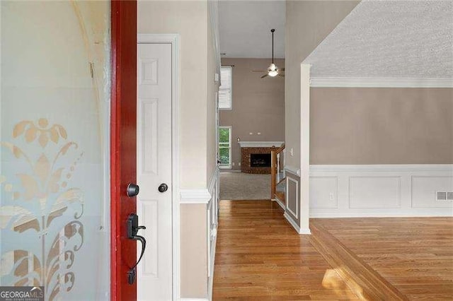 foyer with wood finished floors, visible vents, ornamental molding, a brick fireplace, and ceiling fan
