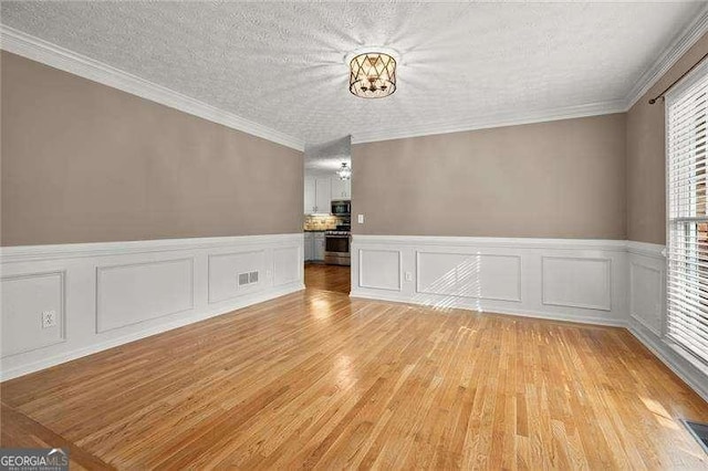 empty room featuring a decorative wall, a wainscoted wall, visible vents, and light wood-type flooring