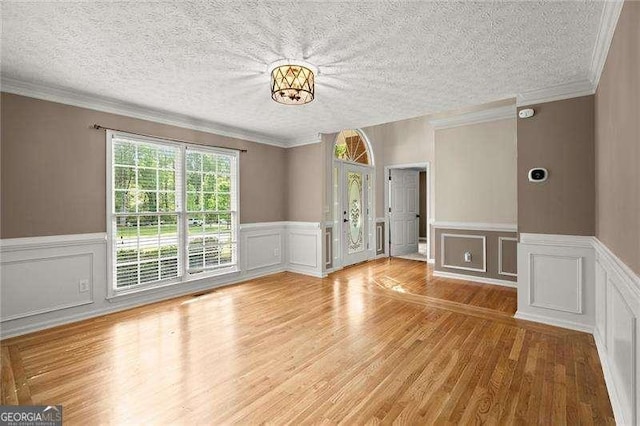 interior space featuring a wainscoted wall, light wood-type flooring, a decorative wall, crown molding, and a textured ceiling