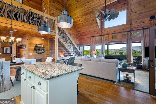 kitchen featuring light wood-type flooring, wooden walls, high vaulted ceiling, and a notable chandelier