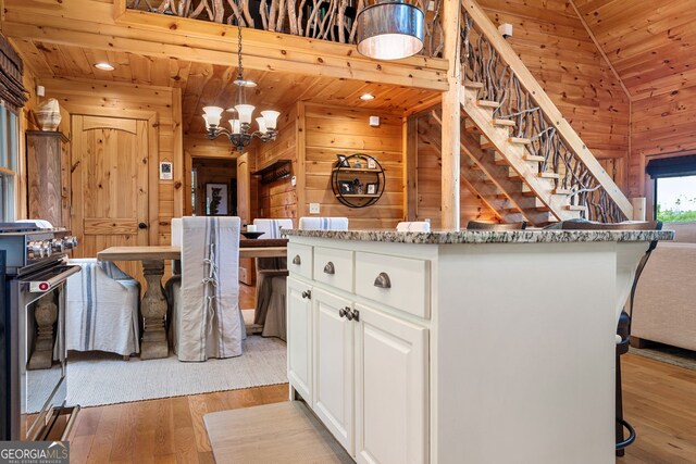 kitchen featuring wooden walls, light wood-type flooring, wood ceiling, stainless steel range with gas stovetop, and white cabinetry