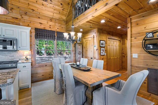 dining area with wood walls, a chandelier, and light wood finished floors