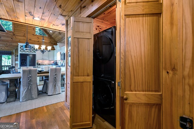 washroom featuring a notable chandelier, wood finished floors, wood ceiling, stacked washing maching and dryer, and laundry area