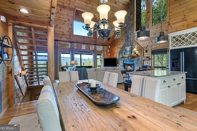 dining area with high vaulted ceiling, a stone fireplace, wood finished floors, a chandelier, and wood walls