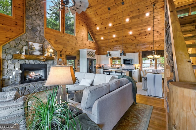 living area featuring high vaulted ceiling, ceiling fan with notable chandelier, wooden walls, light wood-type flooring, and a fireplace