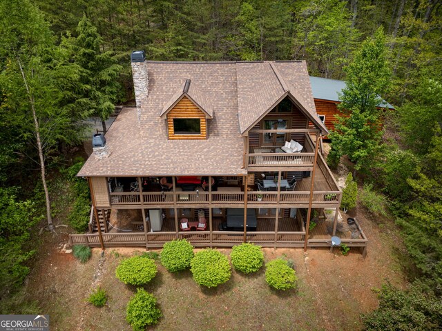 rear view of house with a chimney, stairs, a shingled roof, a balcony, and a forest view
