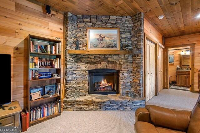 living area featuring a fireplace, carpet, wood walls, and wooden ceiling