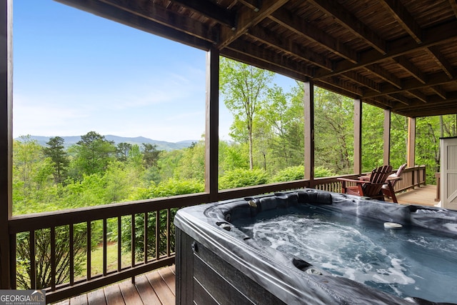 deck with a view of trees, a hot tub, and a mountain view