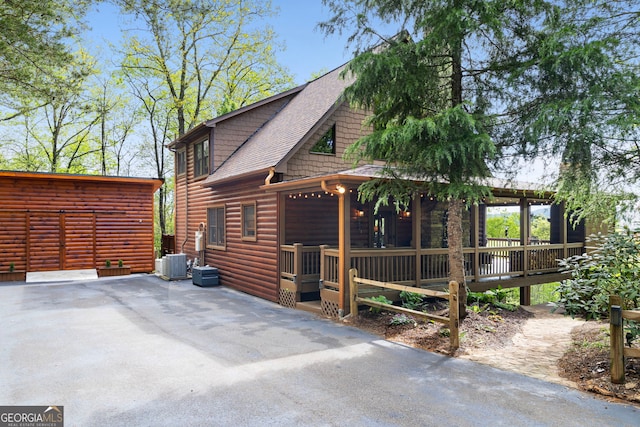 view of side of property featuring roof with shingles, faux log siding, and central air condition unit