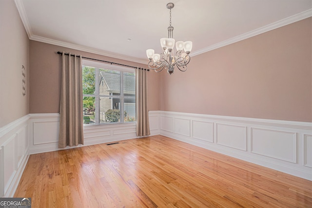 empty room with a chandelier, light wood-type flooring, a wainscoted wall, crown molding, and a decorative wall