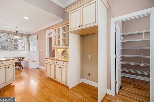 kitchen with cream cabinets, light wood finished floors, crown molding, glass insert cabinets, and light stone countertops