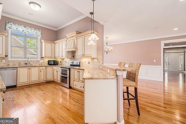 kitchen featuring appliances with stainless steel finishes, cream cabinets, a breakfast bar area, a peninsula, and light wood-type flooring