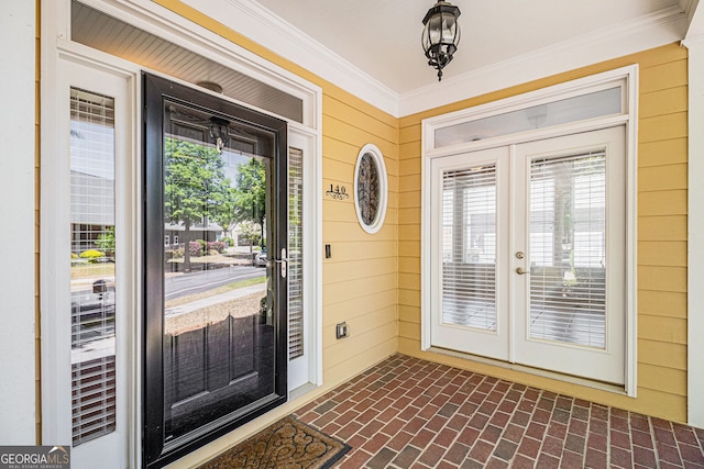 foyer entrance with crown molding, wood walls, brick flooring, and french doors