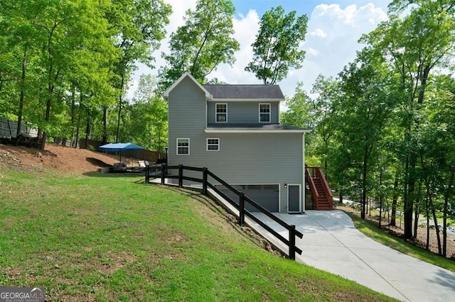 view of side of property featuring fence, stairs, an attached garage, concrete driveway, and a lawn