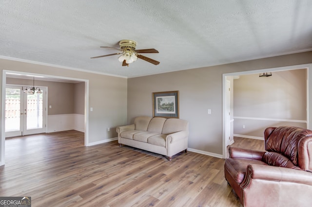 living room featuring light wood-style flooring, a textured ceiling, crown molding, and ceiling fan with notable chandelier