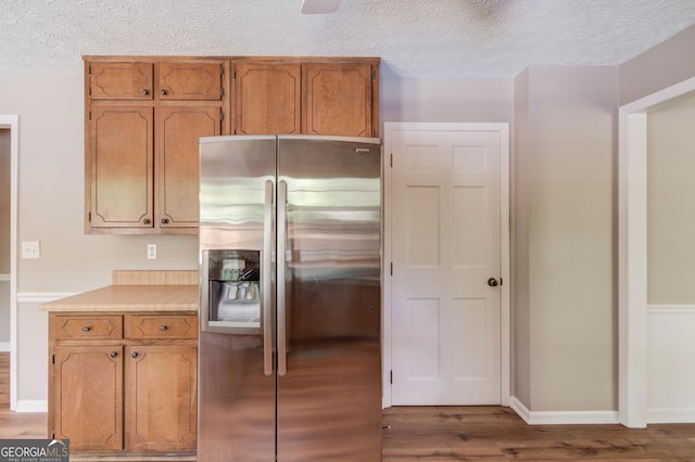 kitchen featuring a textured ceiling, light wood-type flooring, stainless steel fridge with ice dispenser, light countertops, and baseboards