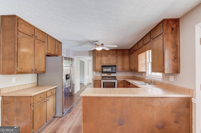 kitchen with light wood finished floors, stainless steel appliances, a peninsula, a sink, and a ceiling fan