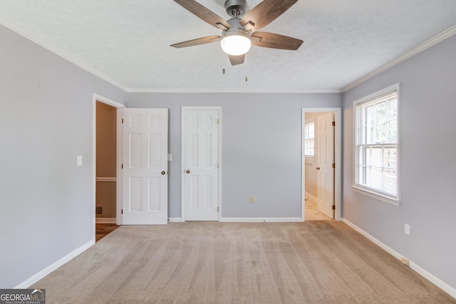 unfurnished bedroom with a textured ceiling, crown molding, baseboards, and light carpet