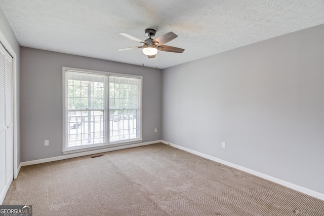 carpeted spare room featuring ceiling fan, baseboards, a textured ceiling, and visible vents