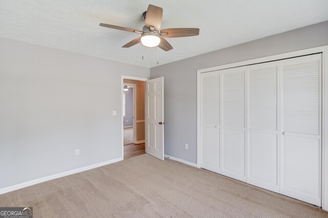 unfurnished bedroom featuring baseboards, light carpet, a ceiling fan, and a closet