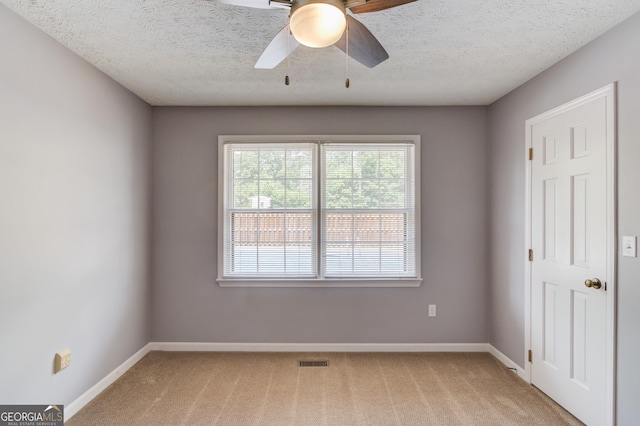 spare room with ceiling fan, visible vents, baseboards, and light carpet