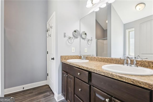 full bath featuring double vanity, a sink, baseboards, and wood finished floors