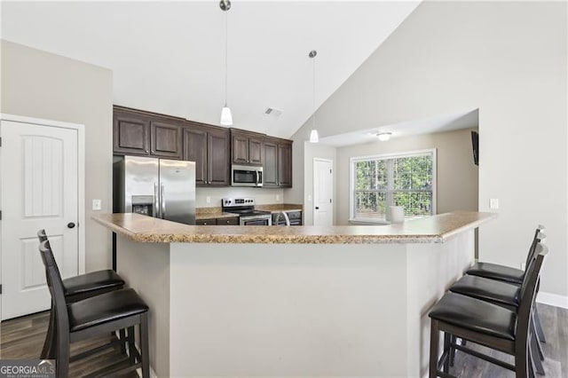 kitchen with dark brown cabinetry, appliances with stainless steel finishes, a kitchen breakfast bar, high vaulted ceiling, and dark wood-style floors