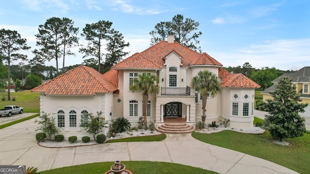 mediterranean / spanish-style house featuring a tile roof, a front lawn, driveway, a chimney, and stucco siding