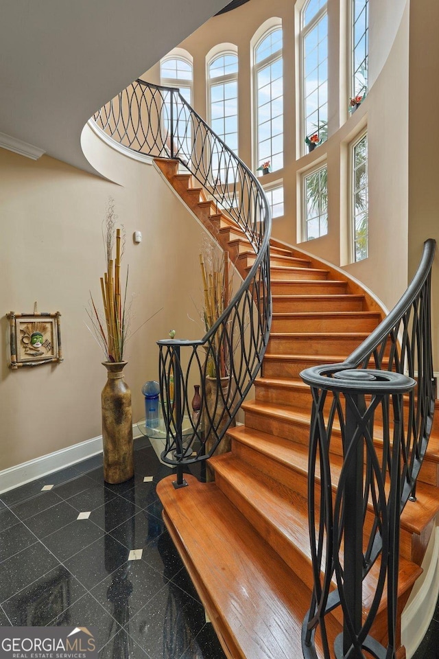 stairs featuring granite finish floor, a high ceiling, and baseboards