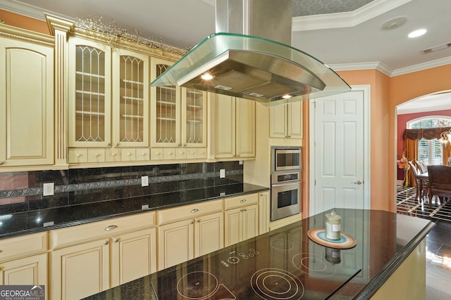 kitchen with cream cabinetry, island exhaust hood, arched walkways, and stainless steel appliances