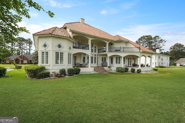 back of house with a tile roof, a patio area, a balcony, a lawn, and a chimney