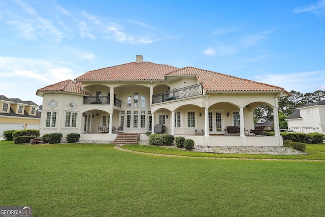 rear view of property with a balcony, a tile roof, a chimney, a lawn, and french doors