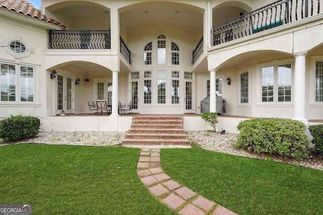back of property featuring a yard, stucco siding, french doors, and a balcony