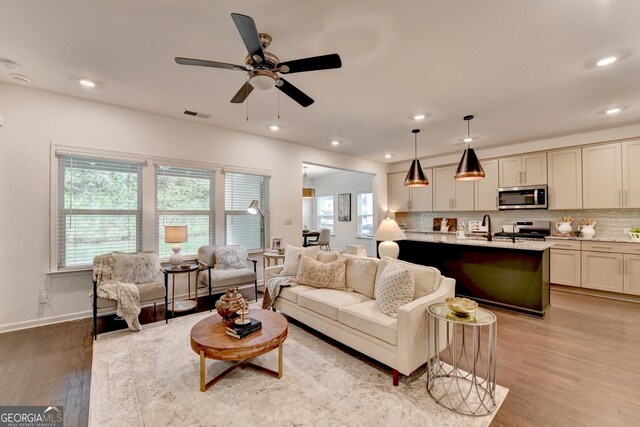 living room with light wood finished floors, a ceiling fan, recessed lighting, and baseboards