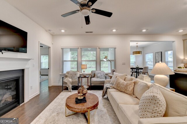 living room with wood finished floors, a ceiling fan, a glass covered fireplace, recessed lighting, and baseboards