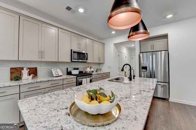 kitchen with appliances with stainless steel finishes, a sink, gray cabinetry, an island with sink, and dark wood-style flooring