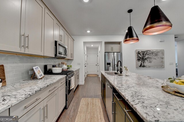kitchen with stainless steel appliances, a sink, light stone countertops, backsplash, and dark wood-type flooring