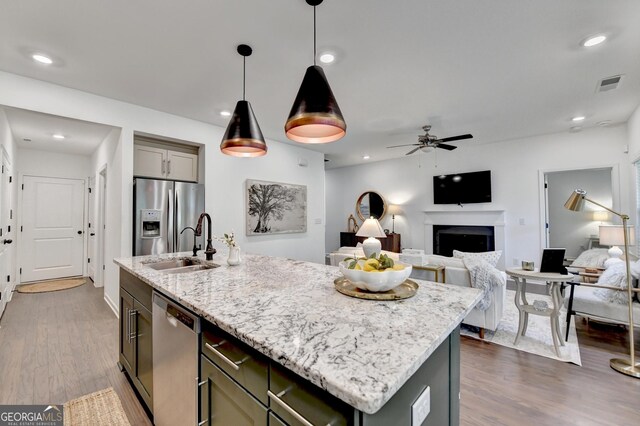 kitchen featuring stainless steel appliances, a fireplace, an island with sink, dark wood finished floors, and recessed lighting